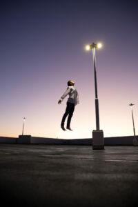 Mann mit Weißen Hemd schwebt dem Licht einer Straßenlaterne entgegen im Sonnenuntergang
