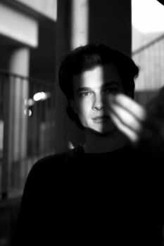 Portrait eines Mannes, Licht fällt durch einen Spalt auf sein Gesicht. Er streicht sich über die Wange, Schwarz Weiß