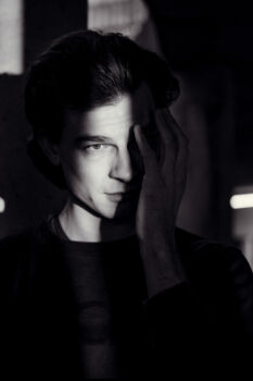 Portrait eines Mannes, Licht fällt durch einen Spalt auf sein Gesicht. Er streicht sich über die Wange, Schwarz Weiß