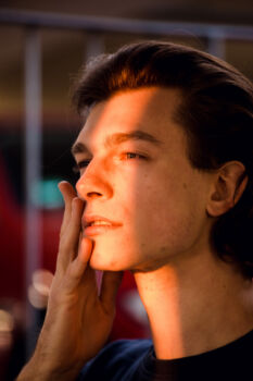 Portrait eines Mannes, Licht fällt durch einen Spalt auf sein Gesicht. Er streicht sich über die Wange